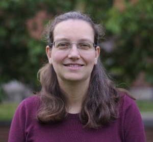professor wearing a purple shirt in front of a forested backdrop